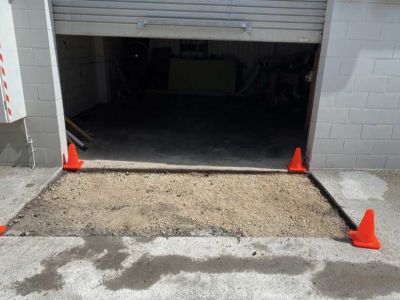 Roller door entry prepared for asphalt patch repair with old pavement removed and base exposed